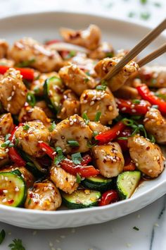 chicken and vegetable stir fry with chopsticks in a white bowl on a table