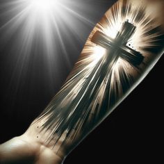 a person's arm with a cross on it and sun shining through the background