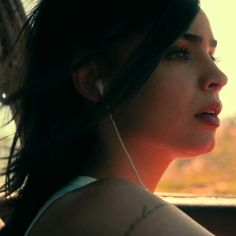 a woman with ear buds in her ears looking out the car window at the sunset