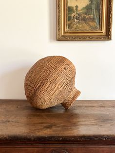 a hat sitting on top of a wooden table in front of a wall with a painting