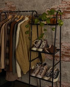 a rack with shoes and sweaters on it in front of a brick wall, next to a potted plant