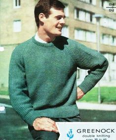 a man in a green sweater is standing on the sidewalk with his hands on his hips