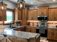 a large kitchen with wooden cabinets and marble counter tops, along with two pendant lights hanging from the ceiling