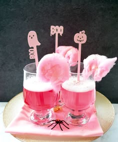 two glasses filled with pink liquid and marshmallows on top of a plate