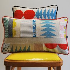 two colorful pillows sitting on top of a wooden stool next to a yellow chair and white wall