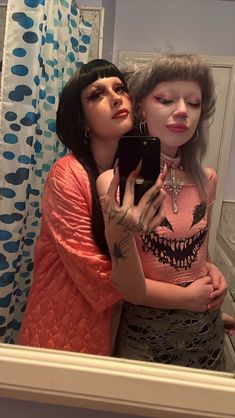 two women standing in front of a mirror taking a selfie with their cell phone