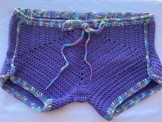 a purple crocheted shorts with blue and green trim on the bottom, sitting on a white surface