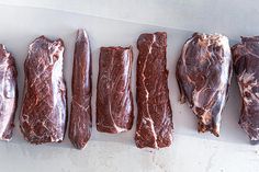 five pieces of raw meat lined up in a row on a white counter top next to each other