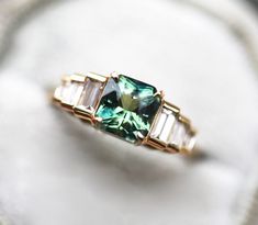 an emerald colored ring with three baguettes in it on a white cloth surface