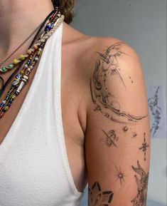 a woman wearing a white tank top with tattoos on her arm and shoulder, looking at the camera