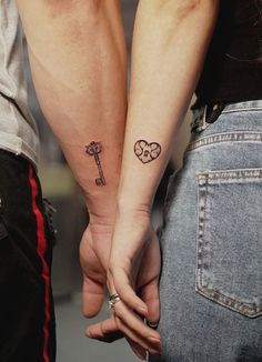 two people holding hands with tattoos on their arms and one has a key to the heart