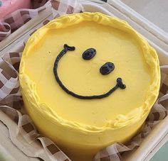 a yellow cake with a smiley face drawn on it's side in a box