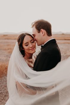 a bride and groom are standing in the desert with their veil blowing in the wind