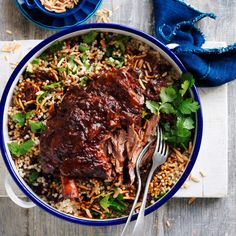 a bowl filled with rice, meat and cilantro on top of a wooden table