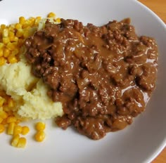 a white plate topped with mashed potatoes and gravy next to corn on the cob