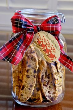 a glass jar filled with cookies on top of a wooden table next to a red bow