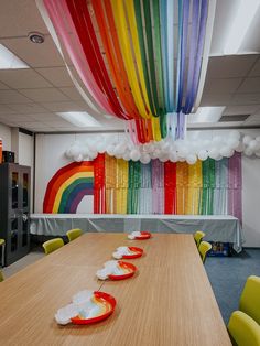 a long table with plates on it in front of a rainbow wall hanging from the ceiling