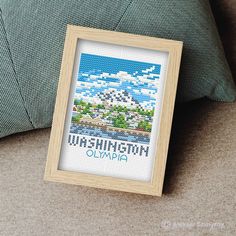 a cross stitch picture frame sitting on top of a couch next to a green pillow