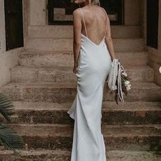 the back of a woman in a white dress standing on some steps with her hands in her pockets