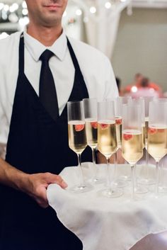 a man holding a tray with wine glasses on it in front of other champagne flutes