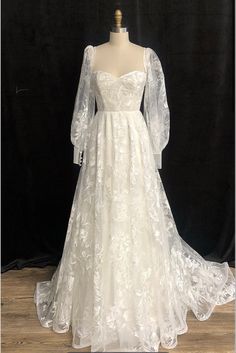 a white wedding dress with long sleeves on a mannequin head stand in front of a black backdrop