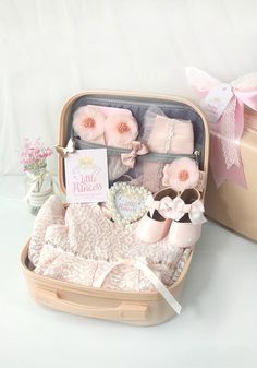 an open suitcase filled with baby items on top of a white table next to a pink box