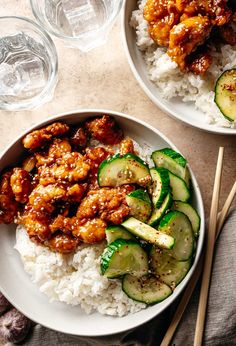 two plates filled with rice, cucumber and chicken on top of each other