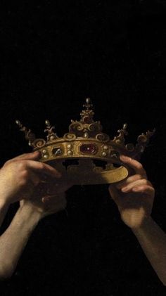 two hands holding up a gold crown in the dark, with one hand on it's face