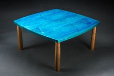 a blue table sitting on top of a gray floor next to a black wall and wooden legs