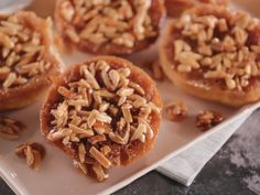 several small pastries on a white plate topped with nuts