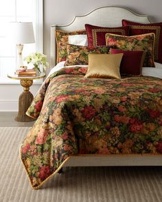 a bed with floral comforter and pillows in a bedroom next to a lamp on a table