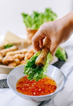 a person dipping some food into a white bowl with lettuce and tomato sauce