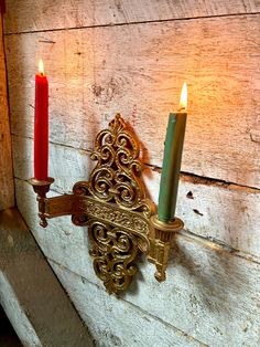 two candles are lit on the wall next to a candle holder with an ornate design