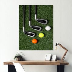 three golf clubs, two balls and an orange on the green grass in front of a table