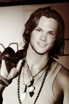 a young man with long hair wearing a necklace and holding his hand up to the camera