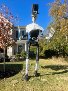 a skeleton with a top hat and cane in front of a house on a sunny day