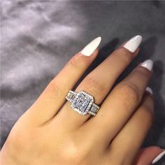 a woman's hand with white nails and a ring on her finger, holding an engagement ring