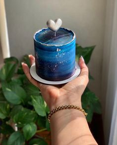 a hand holding a blue cake with a white heart on top