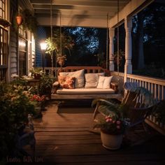 a porch swing with pillows and plants on it at night, lit up by lights