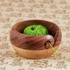 a ball of green yarn in a wooden bowl on a floral tablecloth with a crochet hook