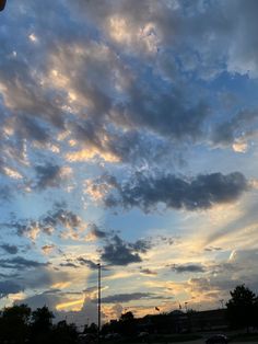 the sky is filled with clouds as the sun goes down in the distance and cars are parked on the side of the road