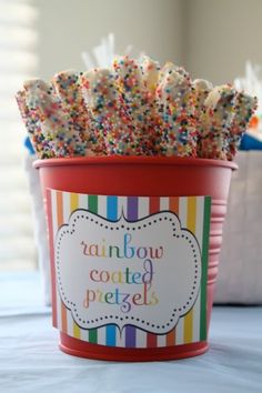 rainbow coated pretzels in a red cup on a blue table with white writing