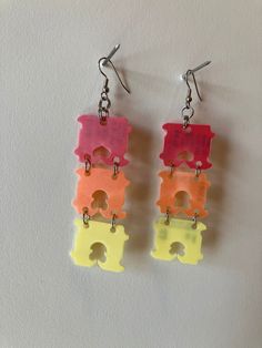 two pairs of colorful plastic earrings hanging from hooks on a white surface, with one pair being cut out and the other part missing