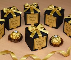 six black boxes with gold ribbon and chocolates wrapped in golden foil are sitting on a table