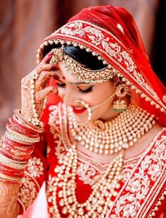 a woman in a red and gold bridal outfit is holding her hands to her face