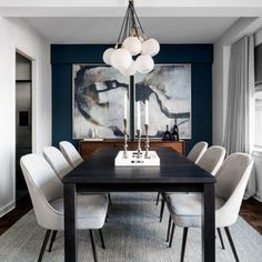 a dining room table with white chairs and a large painting on the wall behind it