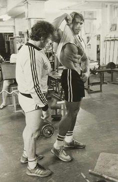 two men standing in a gym with one holding the other's leg while another man holds