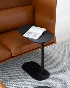 a table with a book on it sitting in front of a brown leather couch and chair