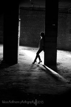 black and white photograph of a woman walking in an empty warehouse with light coming through the windows