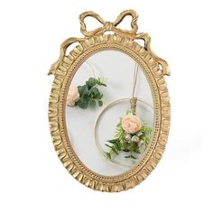 an oval mirror with flowers hanging from it's sides, on a white background